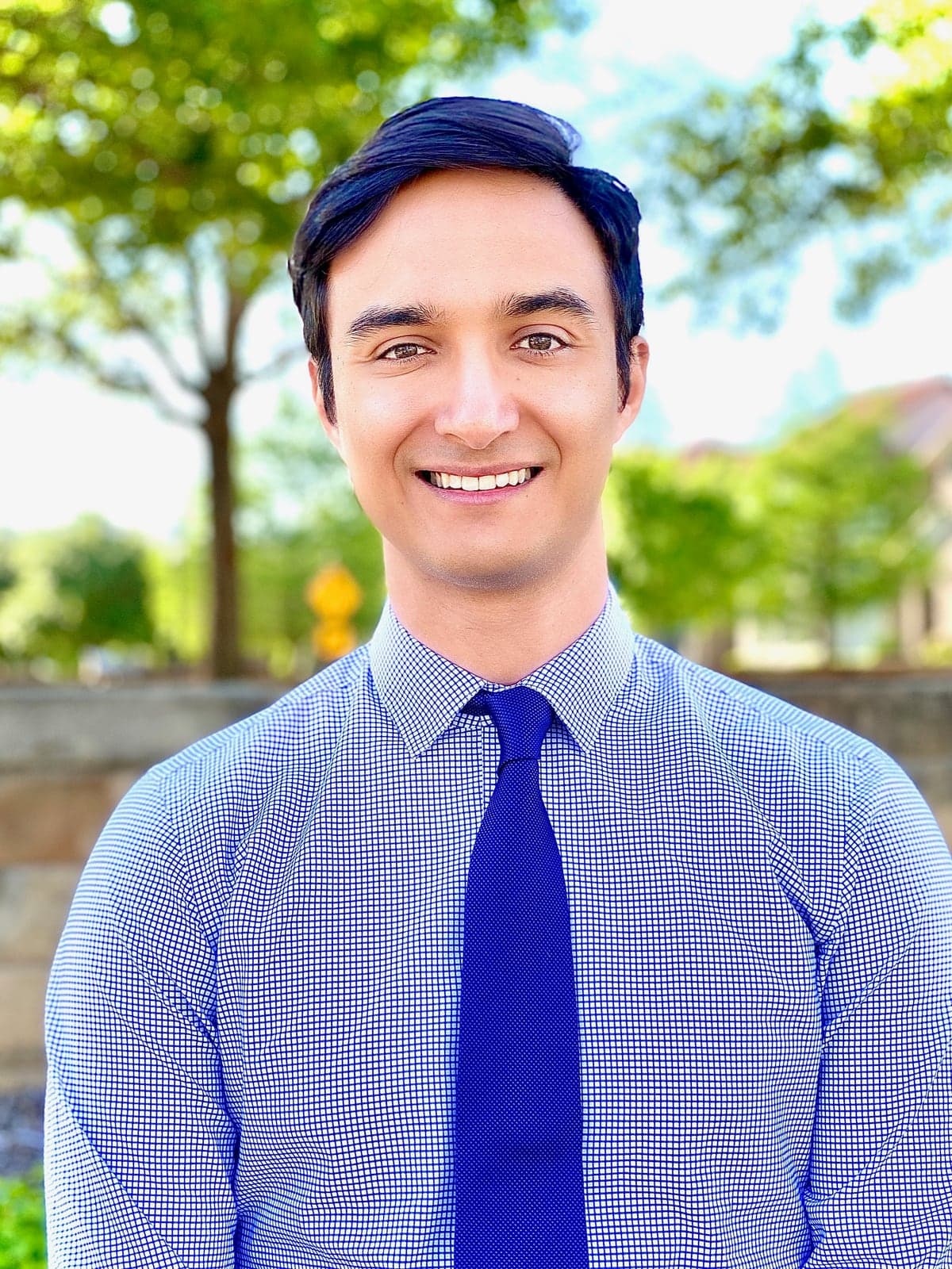 Joseph Carvajales, smiling, in a blue checked shirt and navy tie